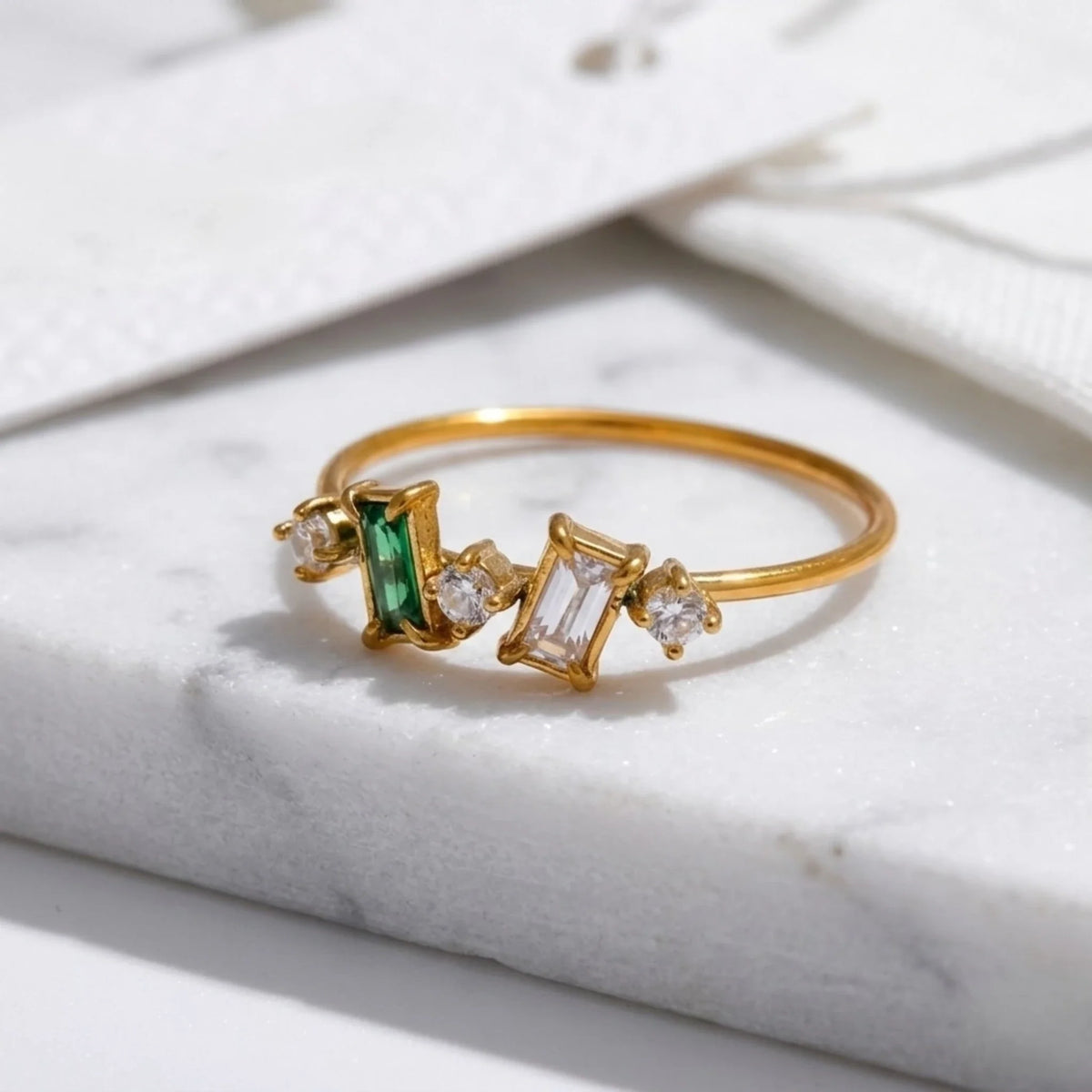 Anello dorato con dettagli smeraldo e diamante su una superficie in marmo