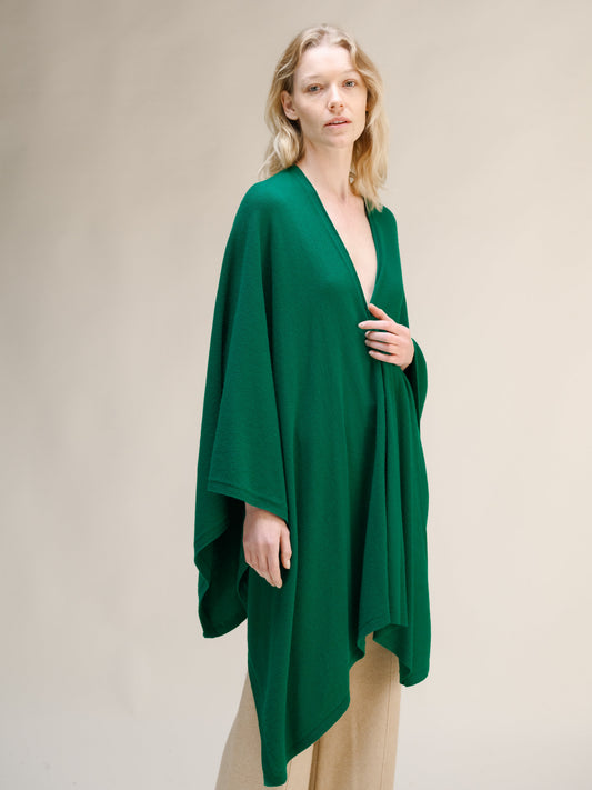 Model wearing emerald green cashmere mix maxi cape with a wrapped front over beige trousers.