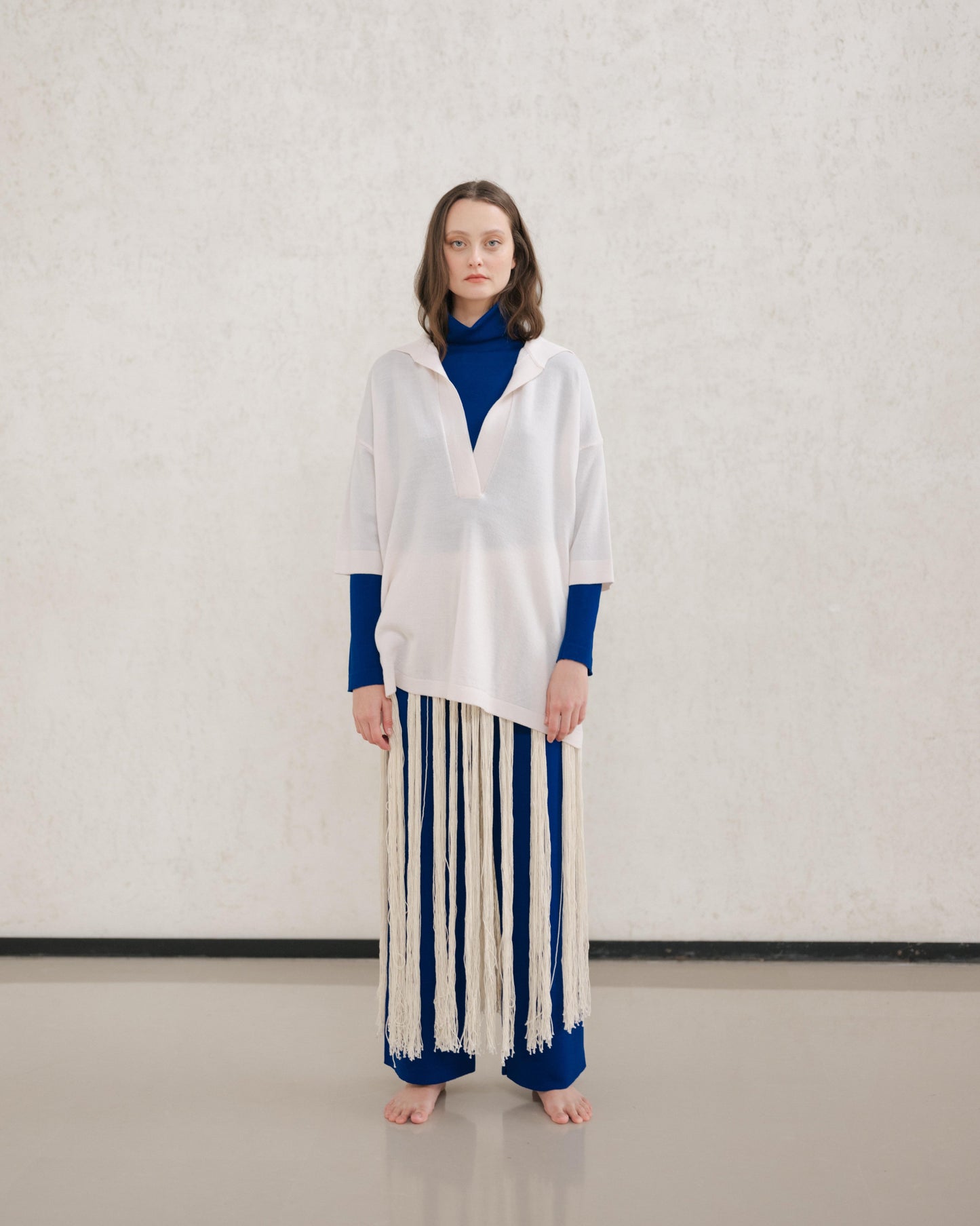 Model wears a pale cream Extra Fine Merino Wool Maxi Polo with a royal blue underlayer and a long fringe skirt.