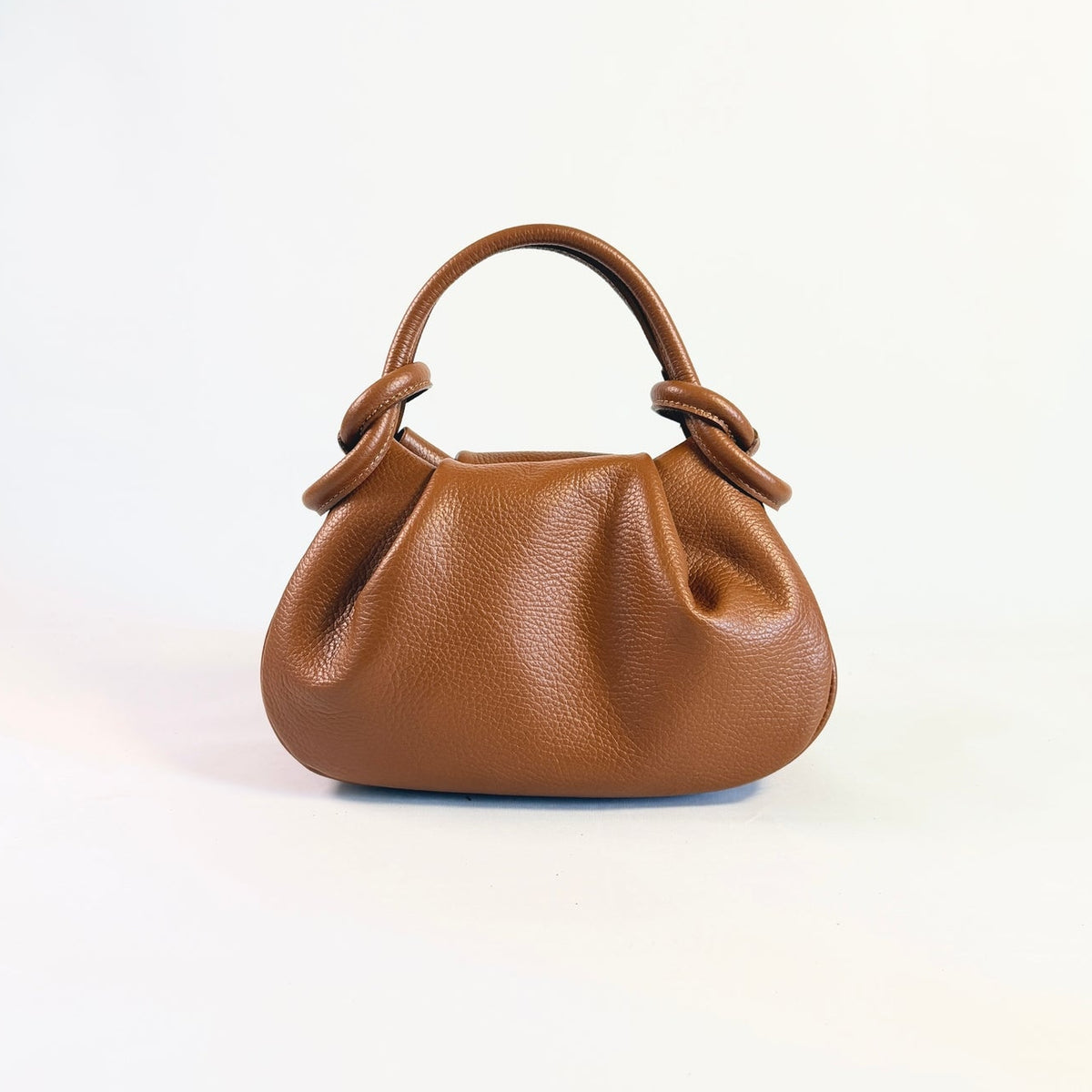 A small cognac anello pebbled leather handbag with a top handle and loop details, photographed against a clean white background.
