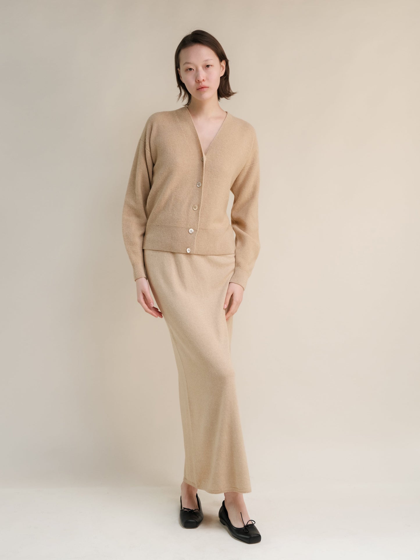 Beige cashmere blend cardigan with a matching high waist long knit skirt worn by a model.