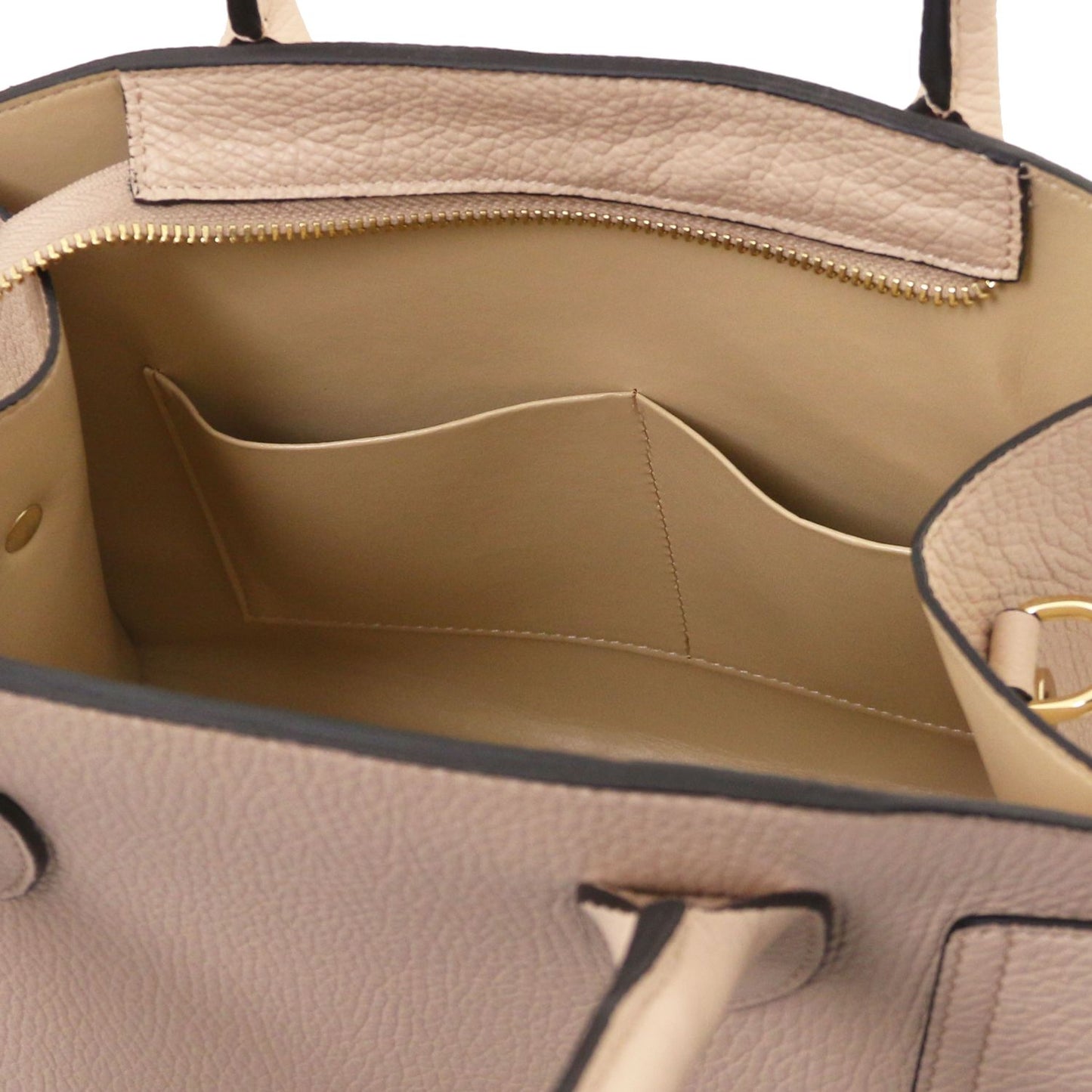 Interior view of beige pebbled leather tote with a gold zipper and curved inner pocket