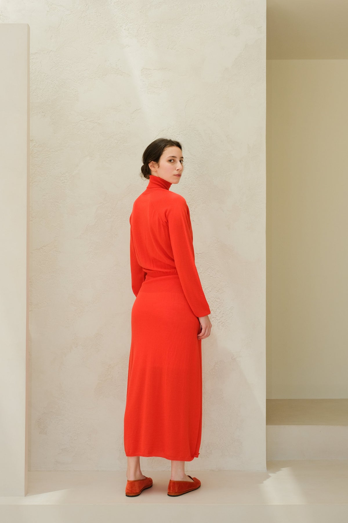 Model draagt felrood merino wool 3D-knit dress with a coltrui, seen from the back.