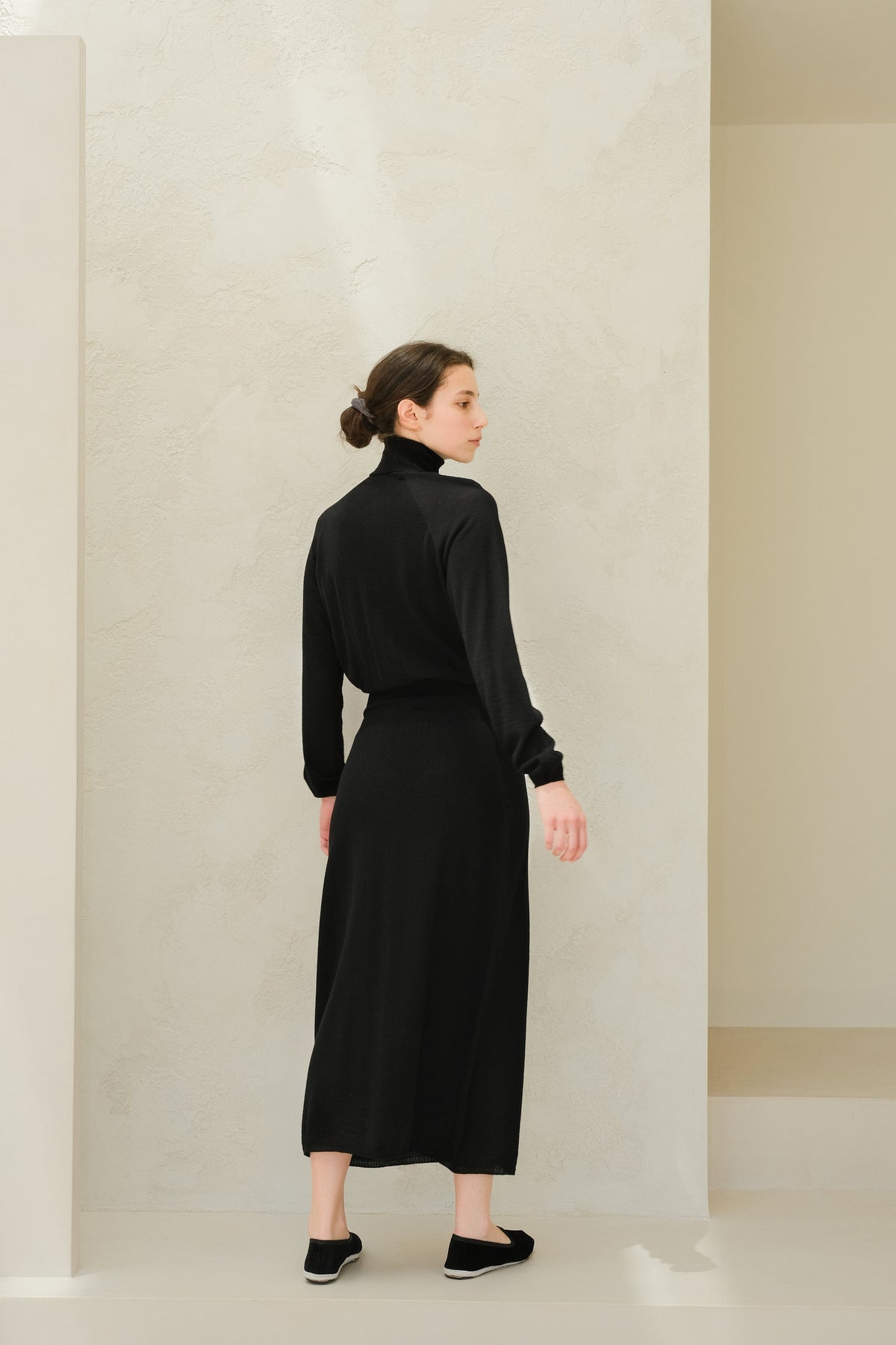 Back view of a model draagt a black 3D knit extra fine merino wool dress with a coltrui and lange mouwen, midi length
