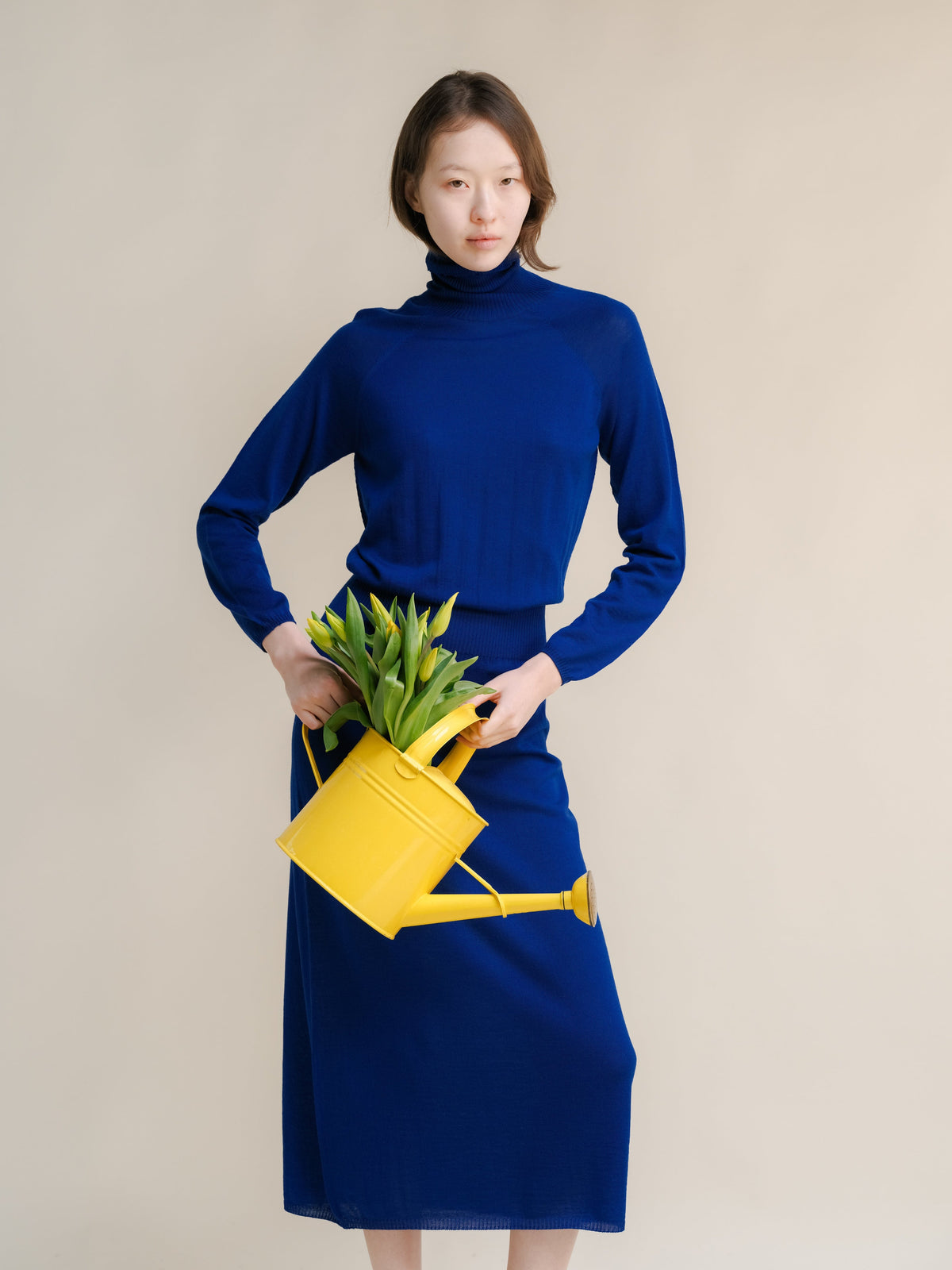 Blue 3D-Knit merino wool dress with coltrui on a model met een gele gieter with tulips