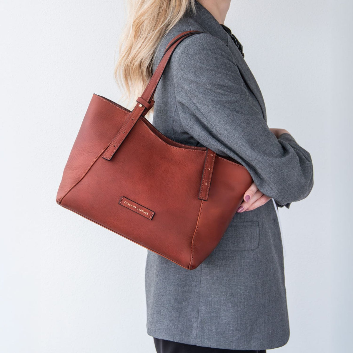 Side view of Libra brown leather tote carried over the shoulder by a model in a gray blazer