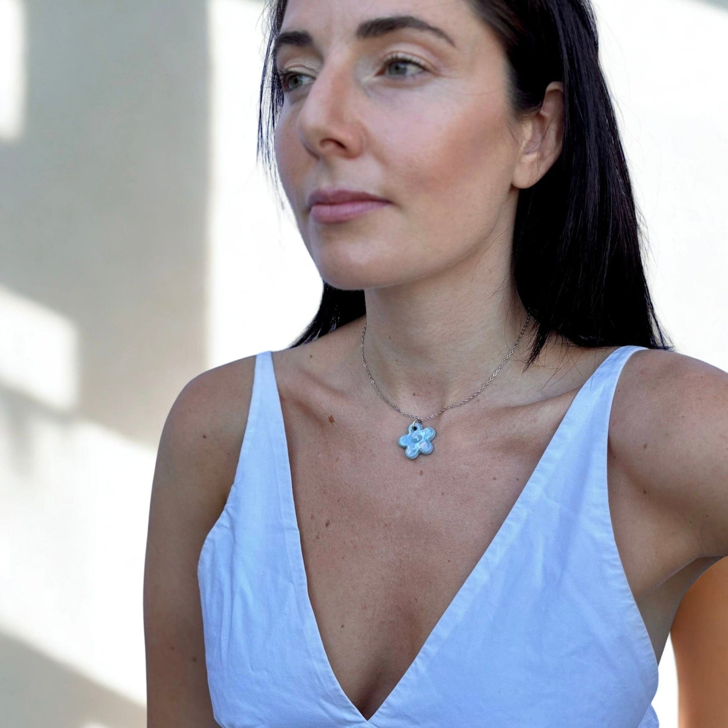 Close-up of a woman wearing a handcrafted pearl light blue floral ceramic pendant necklace