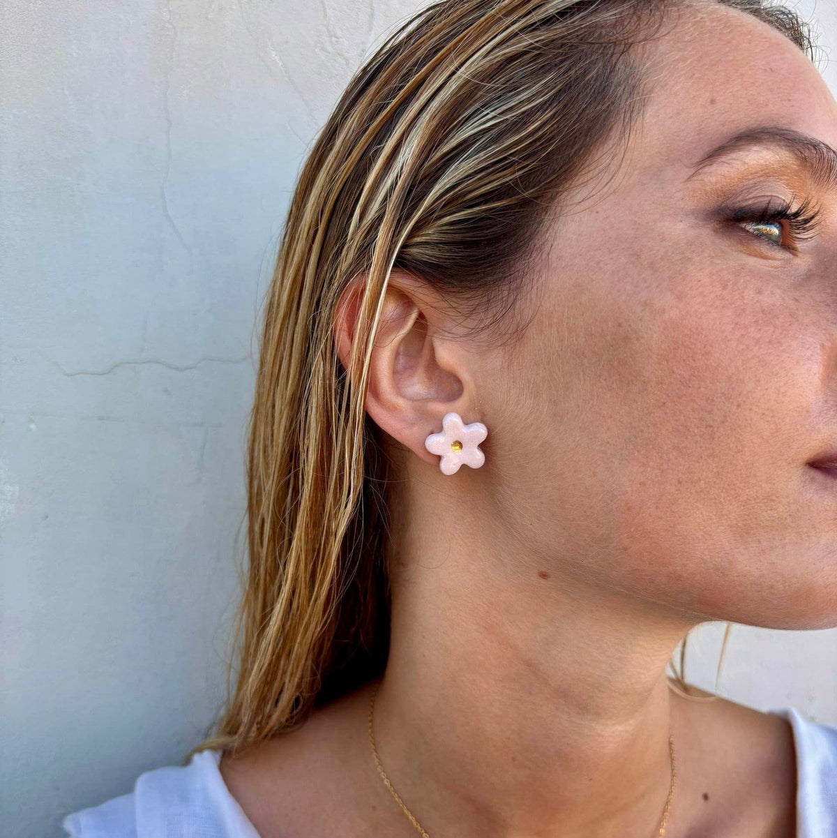 Side view of a pink floral ceramic stud earring with gold center on the model's ear