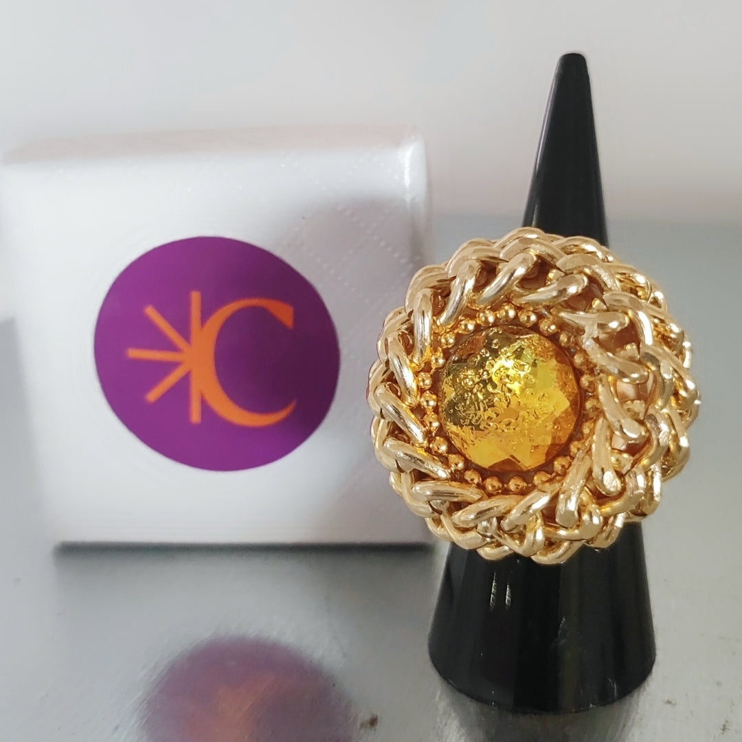Nido di Luce Ring with a yellow center on a black display cone beside a white box with a purple logo.