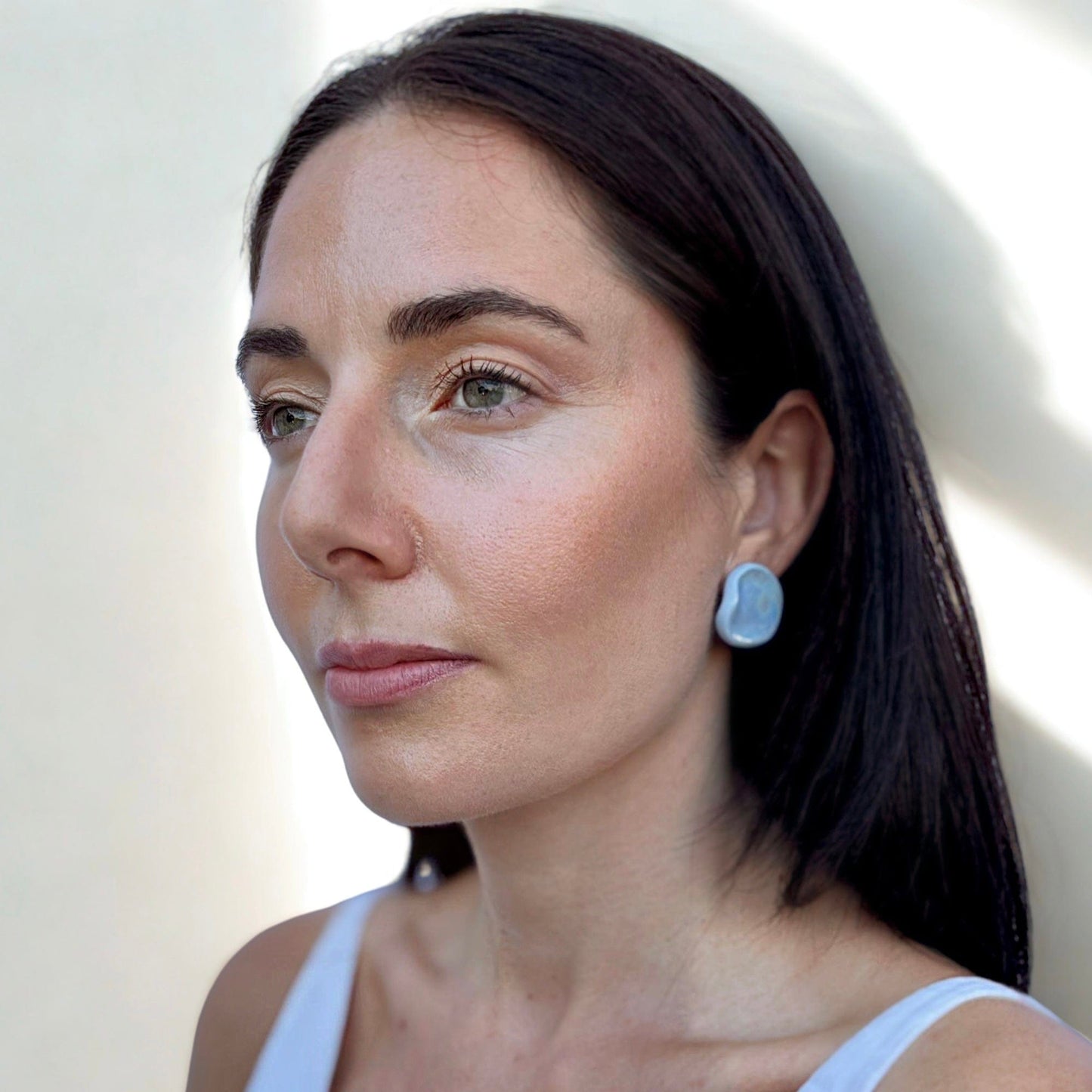 Close-up of a blue ceramic pearl stud earring on a woman's ear from the Perla collection
