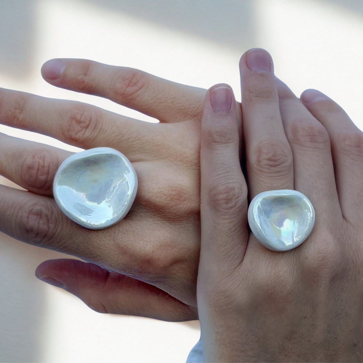 Close up of two hands wearing oversized pearl white ceramic rings from the Perla collection.