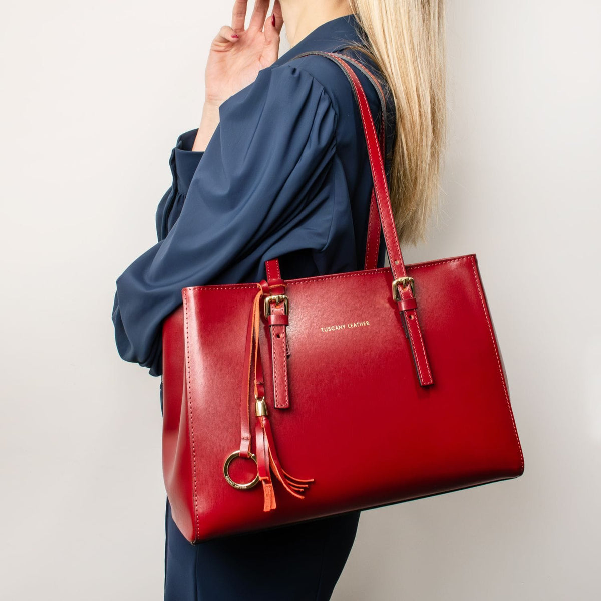 Red handbag with gold accents held by a person wearing a blue outfit on a light gray background