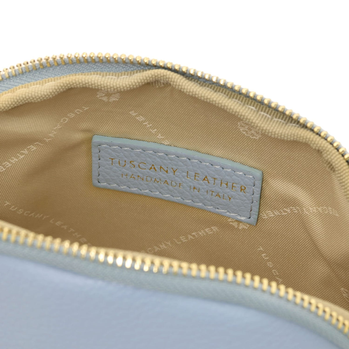 Gros plan of a cuir souple toiletry case interior showcasing beige doublure en tissu and stitched Tuscany Leather label inside zipper closure.