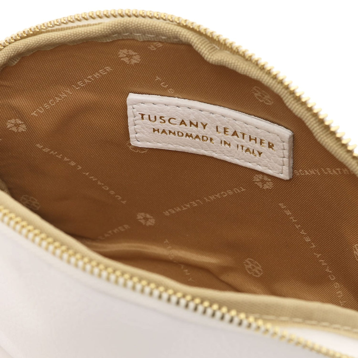 Gros plan of beige leather toiletry case interior featuring branded doublure en tissu and stitched Tuscany Leather label inside zipper opening.