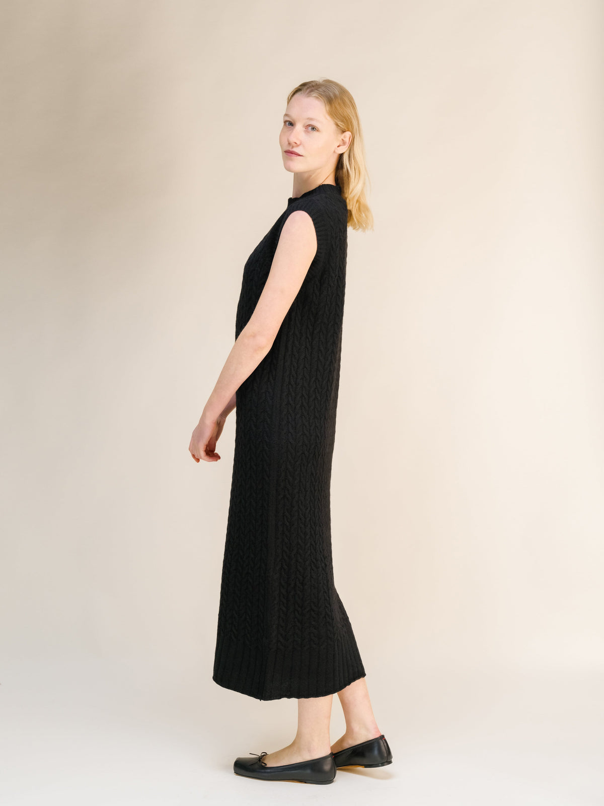 Side view of a black Wool & Cashmere Mix Sleeveless Cable Knit Dress with a ribbed hem and high neckline