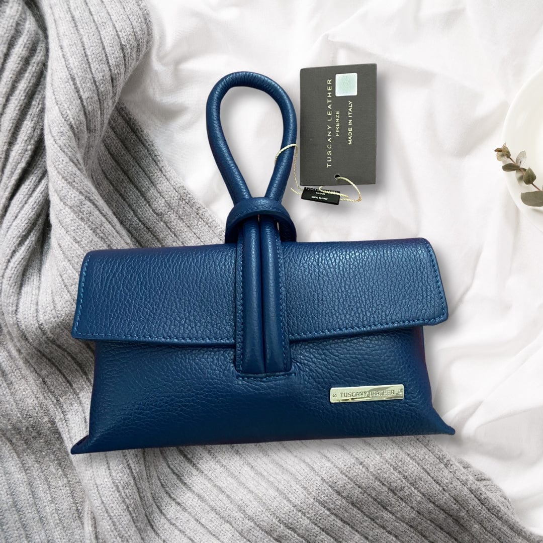 Blue TL Bag by Tuscany Leather, displayed on a soft grey knit fabric with product tag visible – elegant Italian leather accessory.