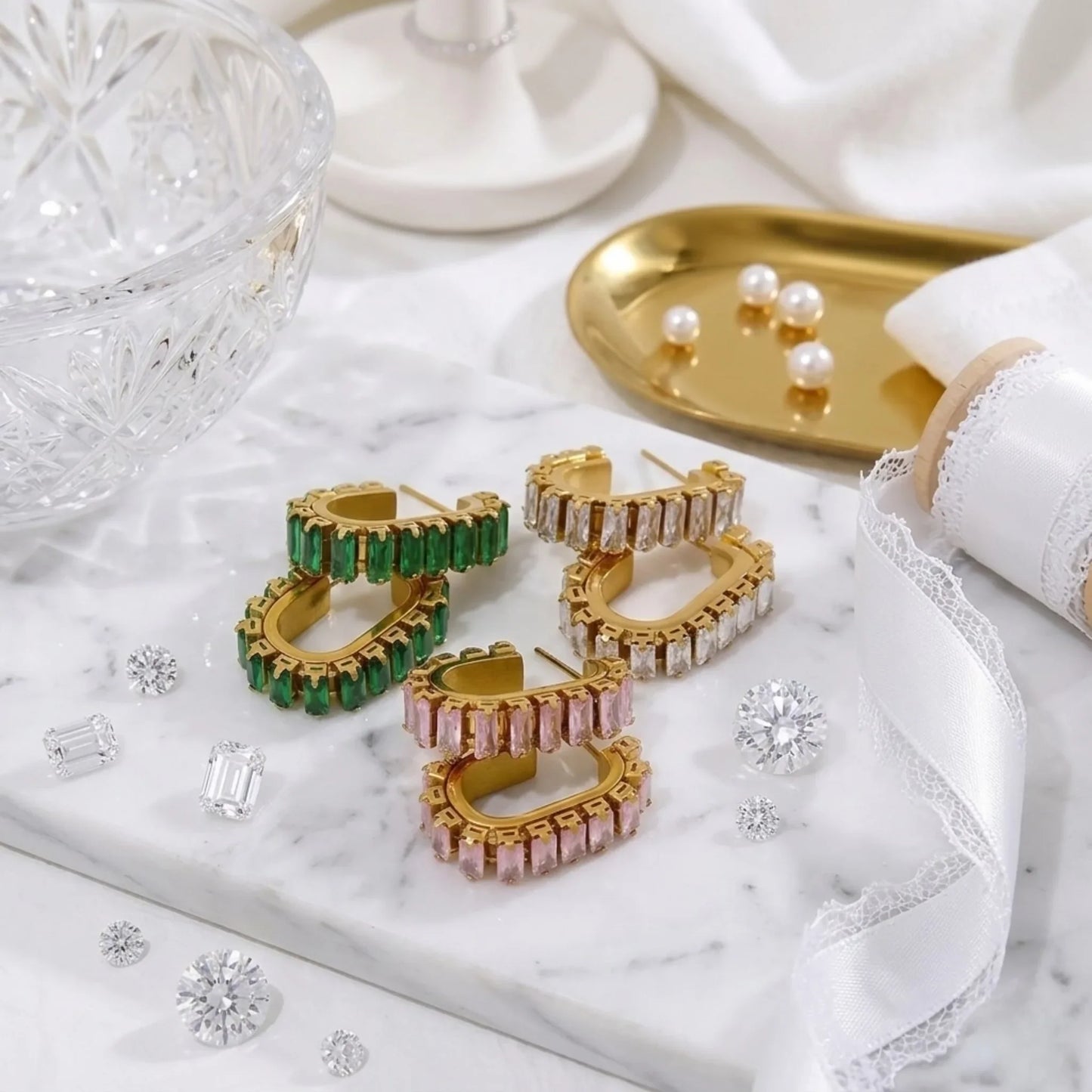 Gold hoop earrings with green and pink gemstones on a marble surface.