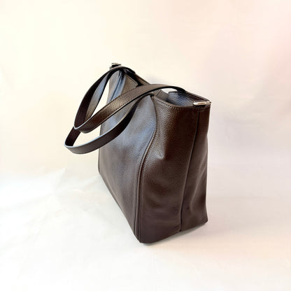A dark brown pebbled leather tote bag with a single shoulder strap, shown from a side angle on a plain white background.