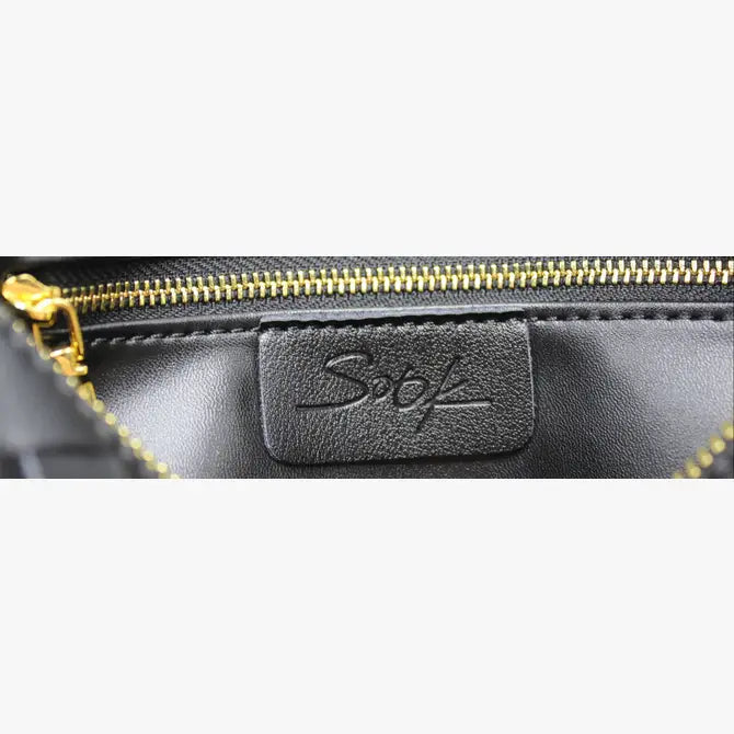 Interior close up of black woven leather pouch with gold zipper and embossed logo patch