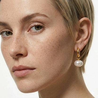Close-up of a woman wearing a gold earring with a pearl drop on a white background