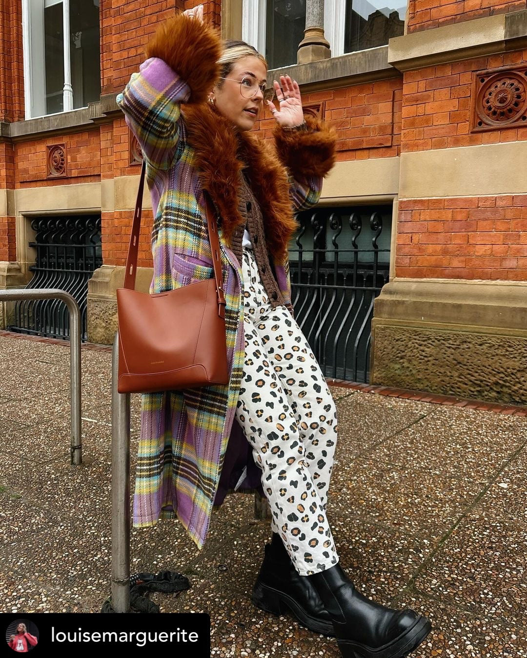 Woman in stylish outfit with fur coat, plaid scarf, and leopard print pants standing on a street.