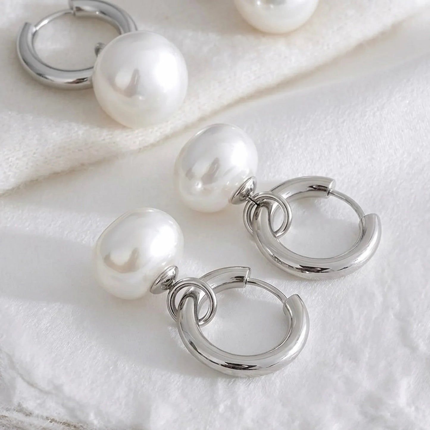 Silver hoop earrings with pearl beads on a white fabric background