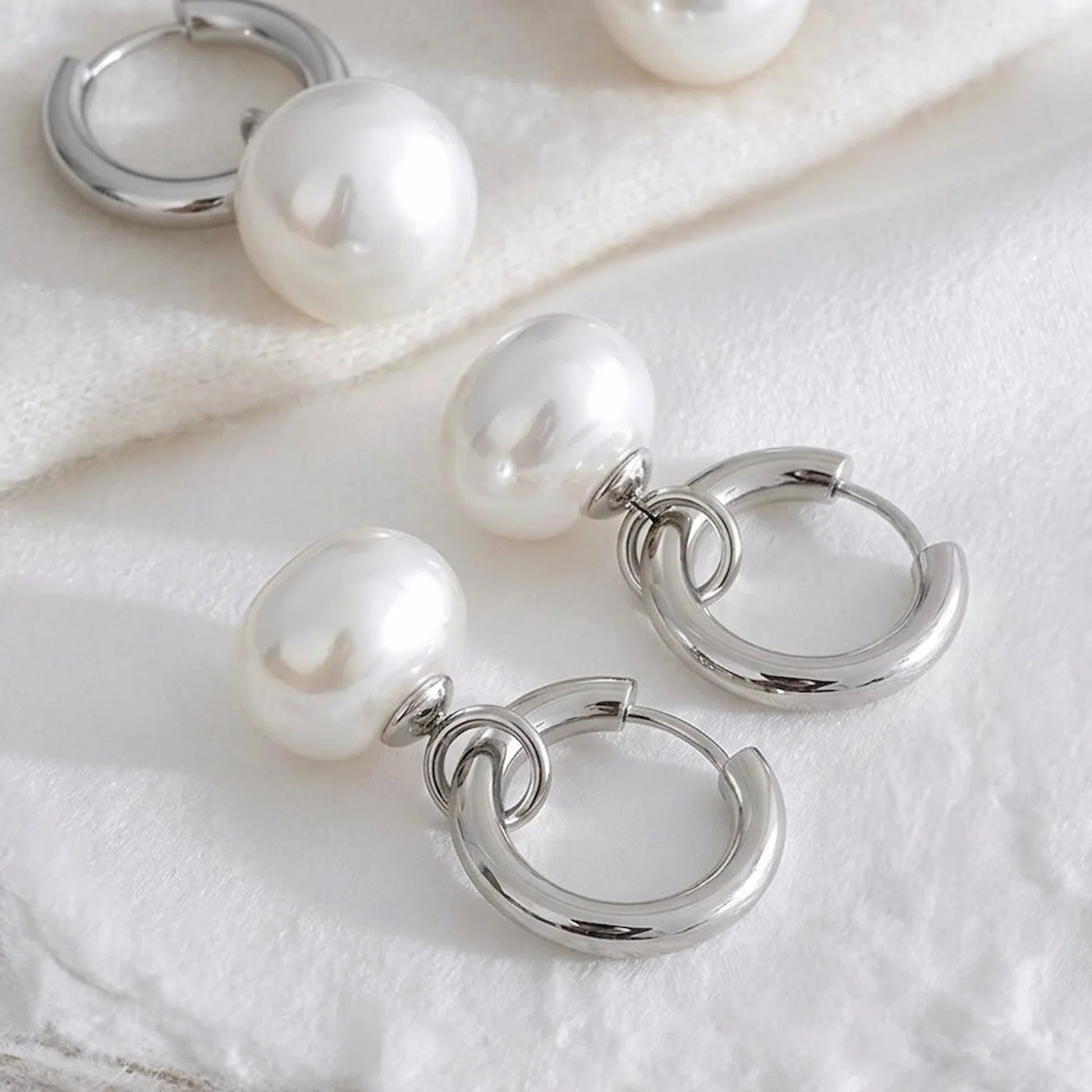 Silver hoop earrings with pearl beads on a white fabric background