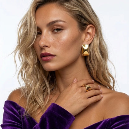 Woman wearing gold earrings and ring, with a purple top against a white background
