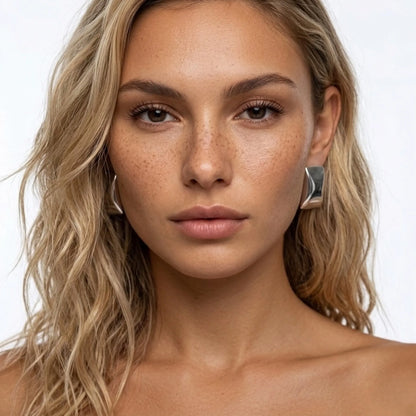 Close-up of a woman with blonde hair and freckles wearing silver earrings on a white background