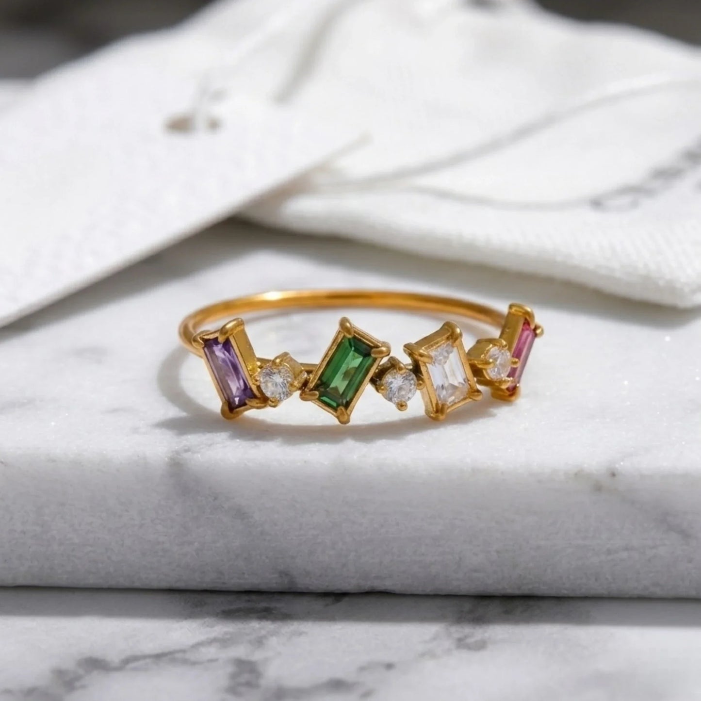 Gold ring with colorful gemstones on a marble surface