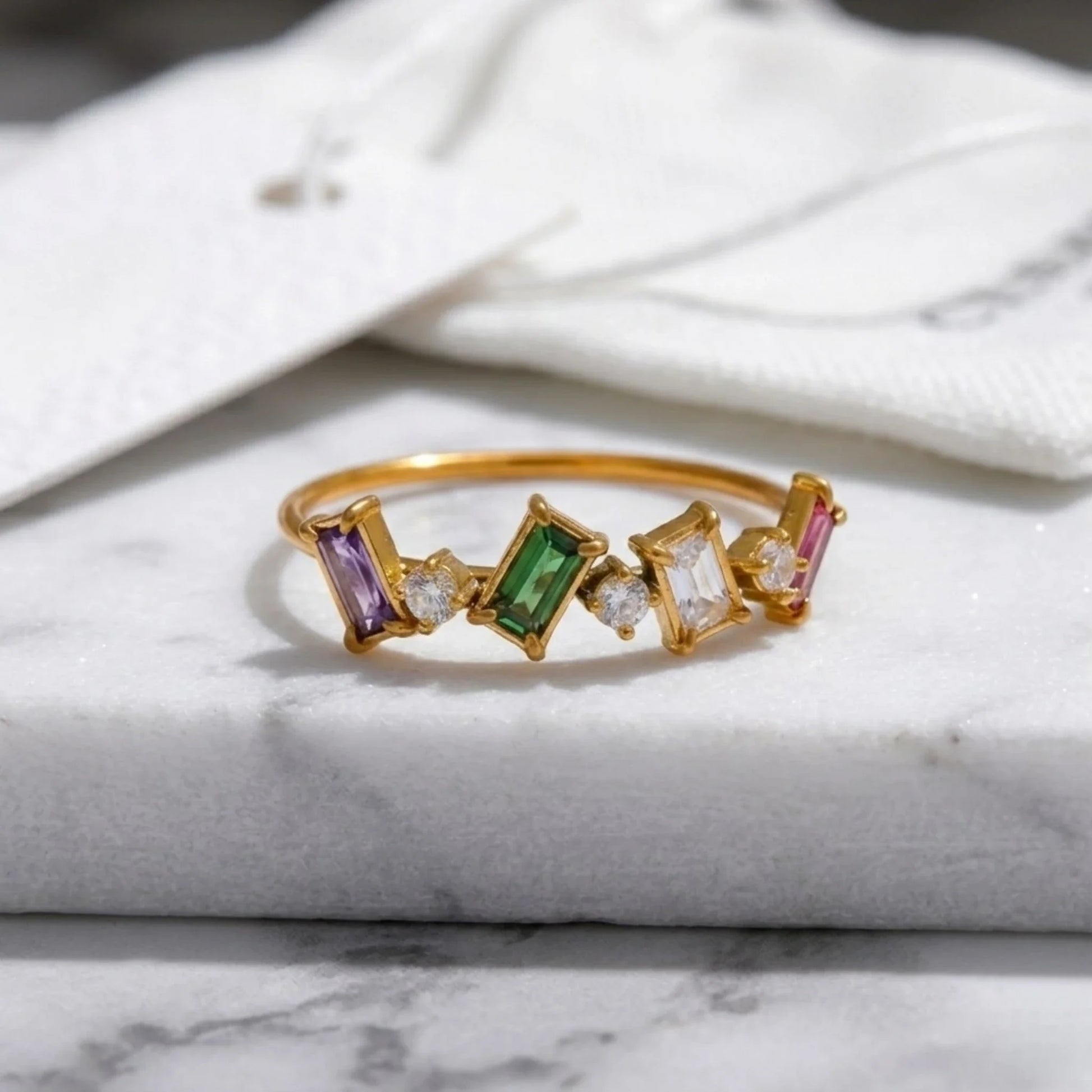 Gold ring with colorful gemstones on a marble surface