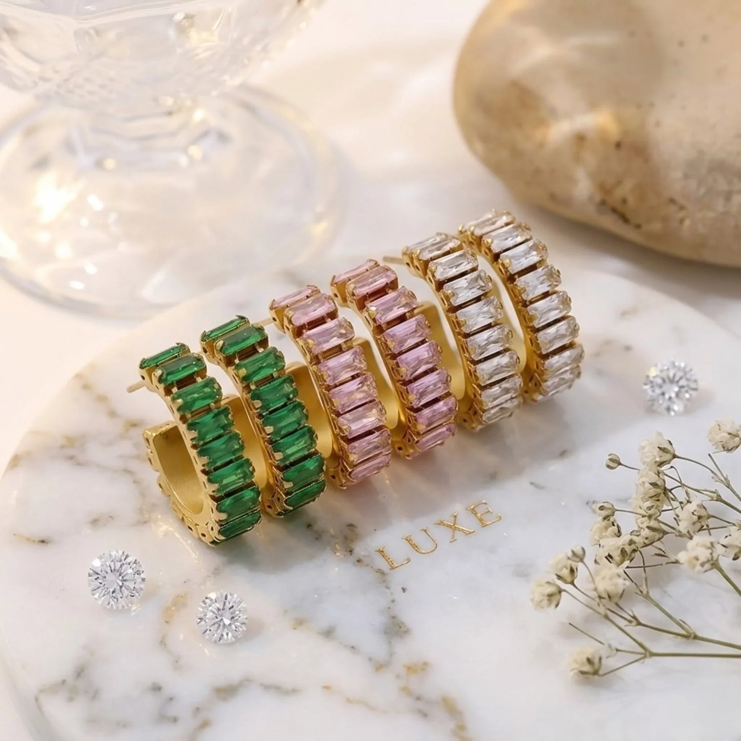 Set of gold earrings with green, pink, and clear gemstones on a marble surface.