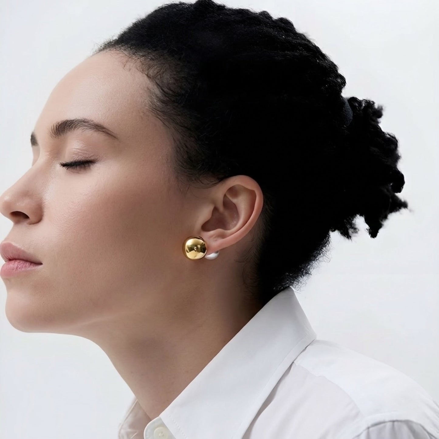 Woman wearing gold earrings with a pearl back on a white background
