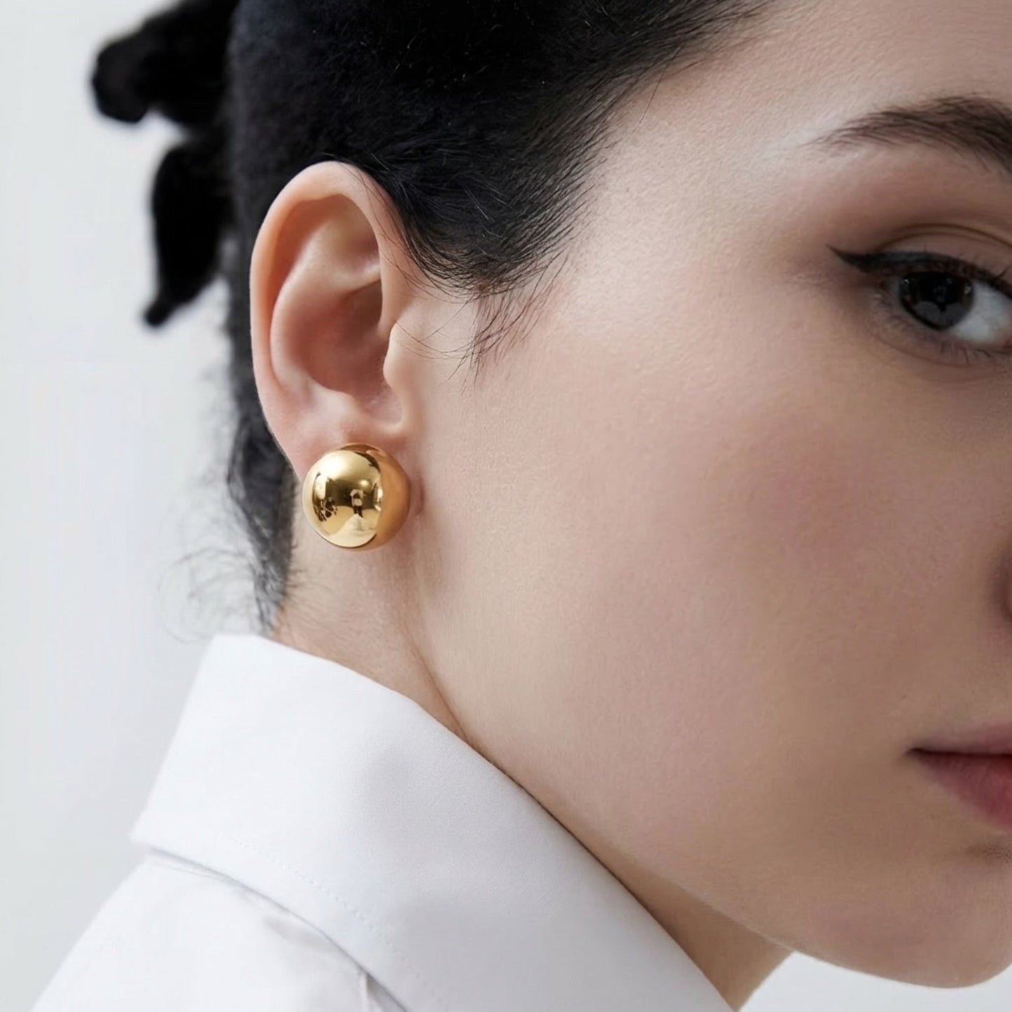 Close-up of a person wearing gold earrings with a neutral background