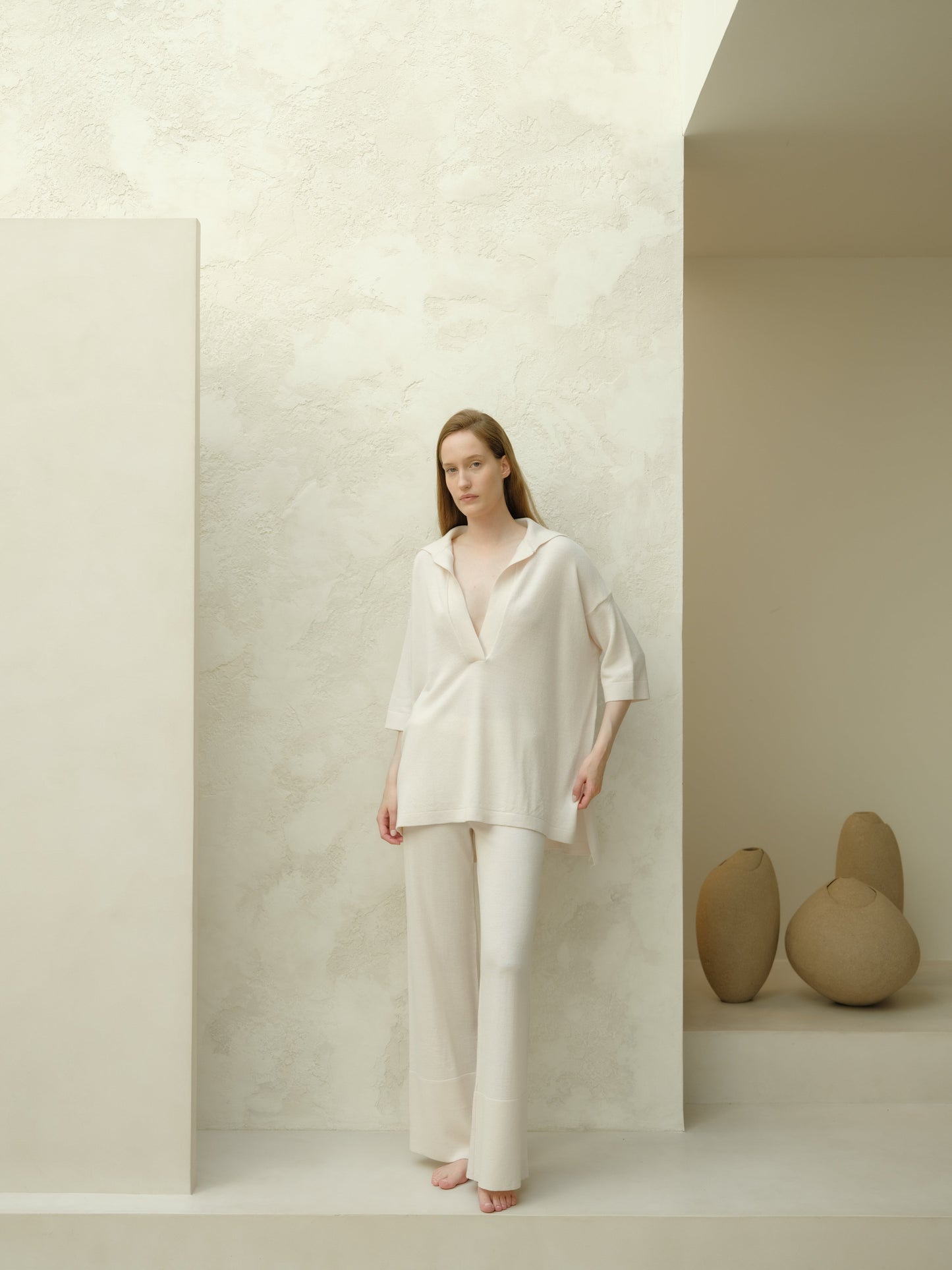 Full body view of a model in an off white Extra Fine Merino Wool Maxi Polo paired with matching wide leg pants in a minimalist studio.