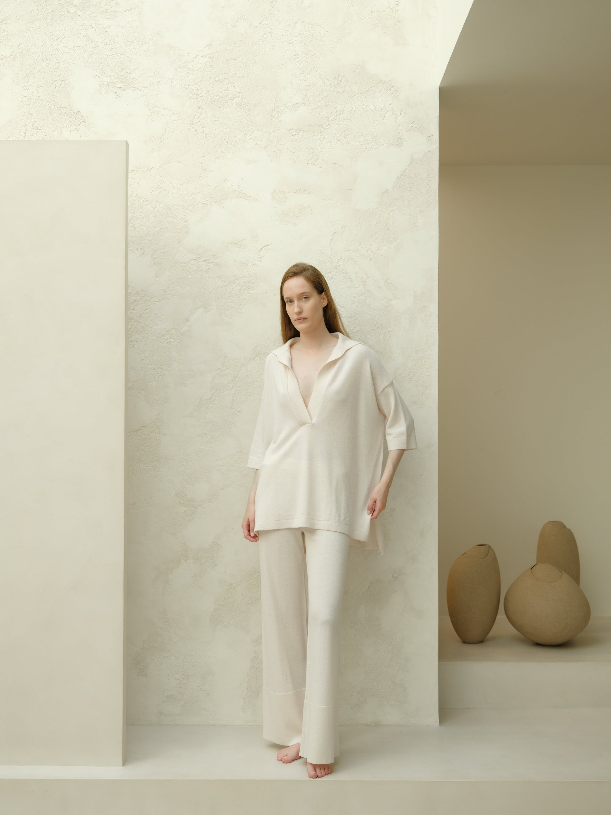 Full body view of a model in an off white Extra Fine Merino Wool Maxi Polo paired with matching wide leg pants in a minimalist studio.