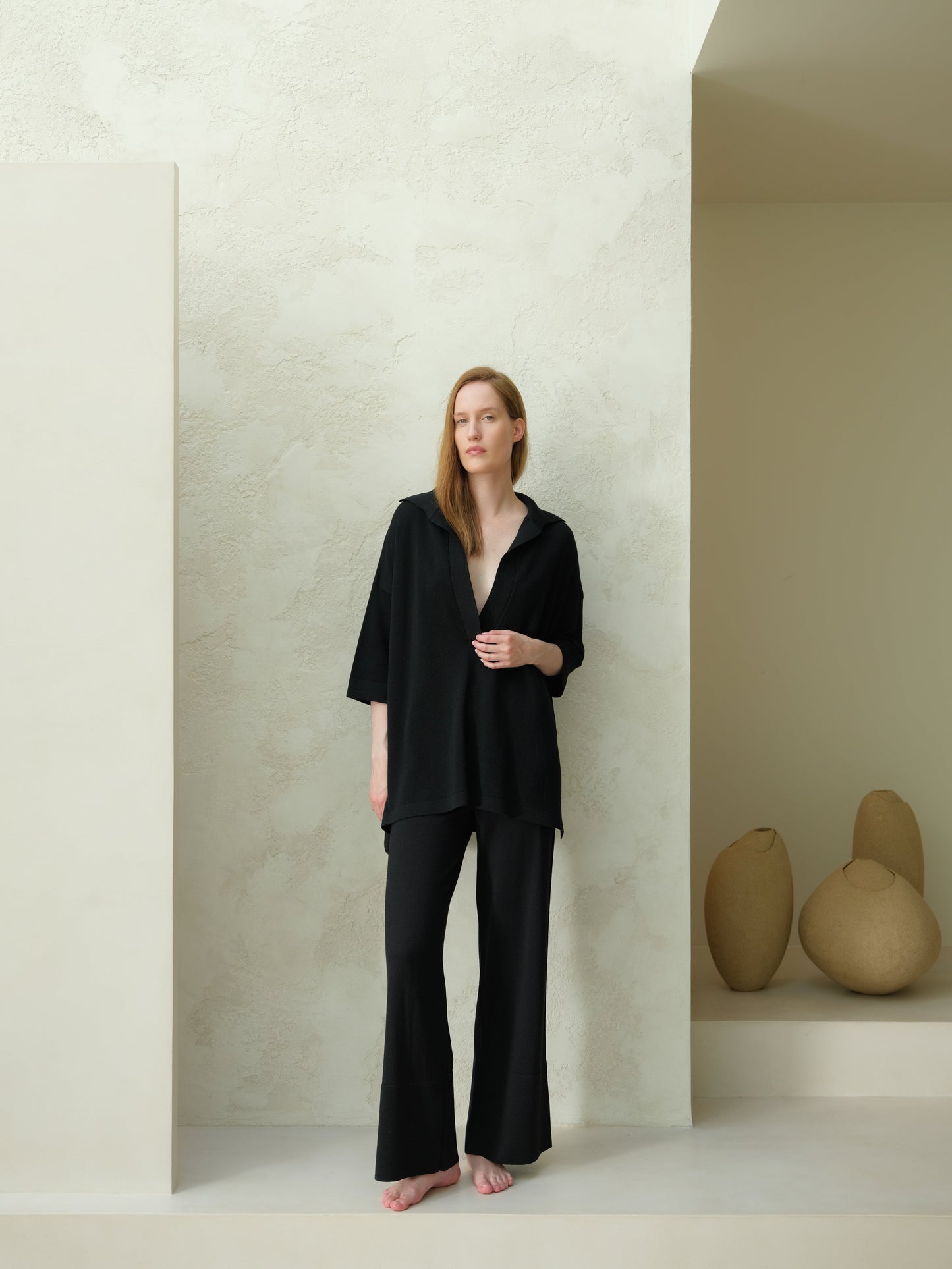 Full-body view of a model in a black Extra Fine Merino Wool Maxi Polo paired with wide-leg pants in a minimalist studio.