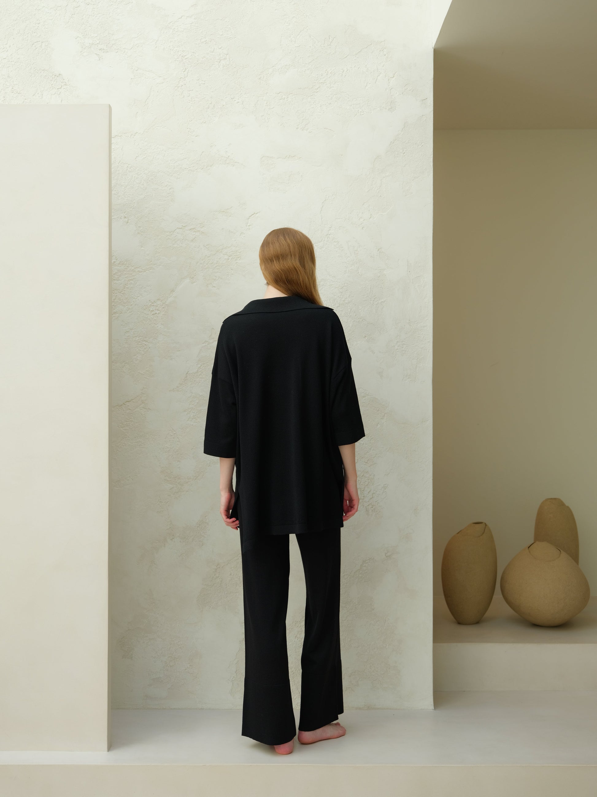 Back view of a model wearing a black Merino Wool Maxi Polo with an oversized silhouette