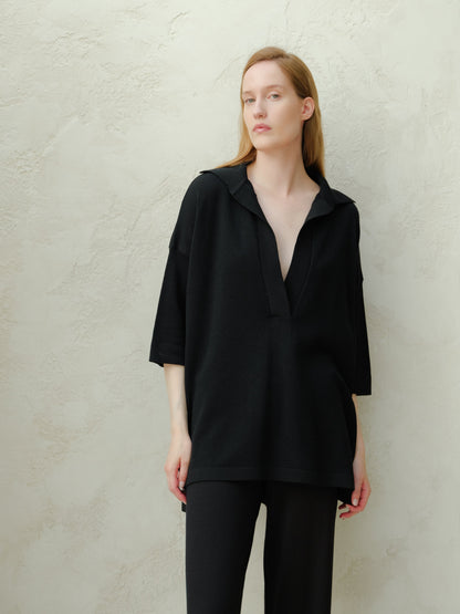 Woman in black oversized merino wool maxi polo with deep V-neck and relaxed silhouette.