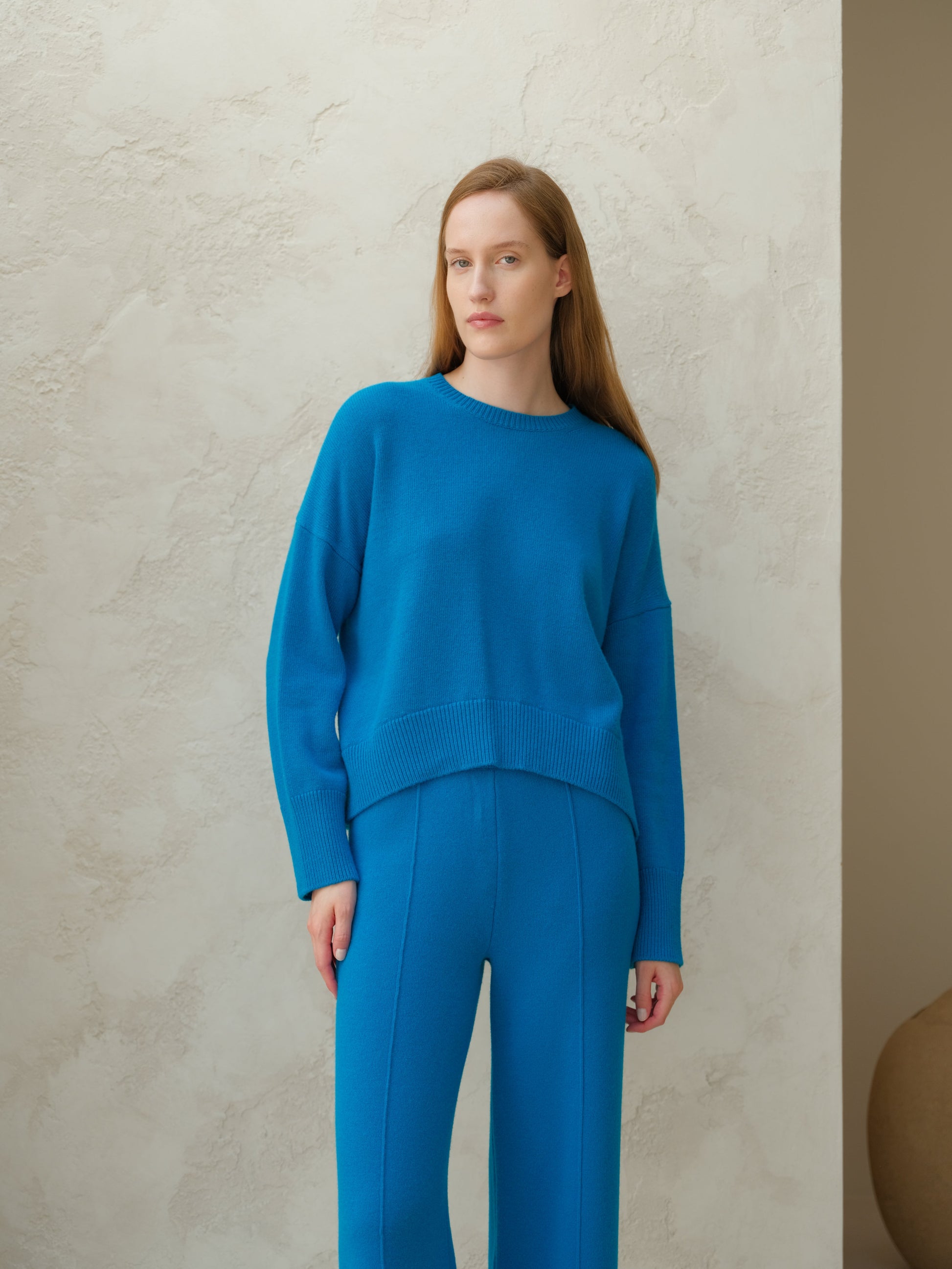 Model wearing bright blue cashmere mix crewneck sweater with matching blue knit pants against a light wall.