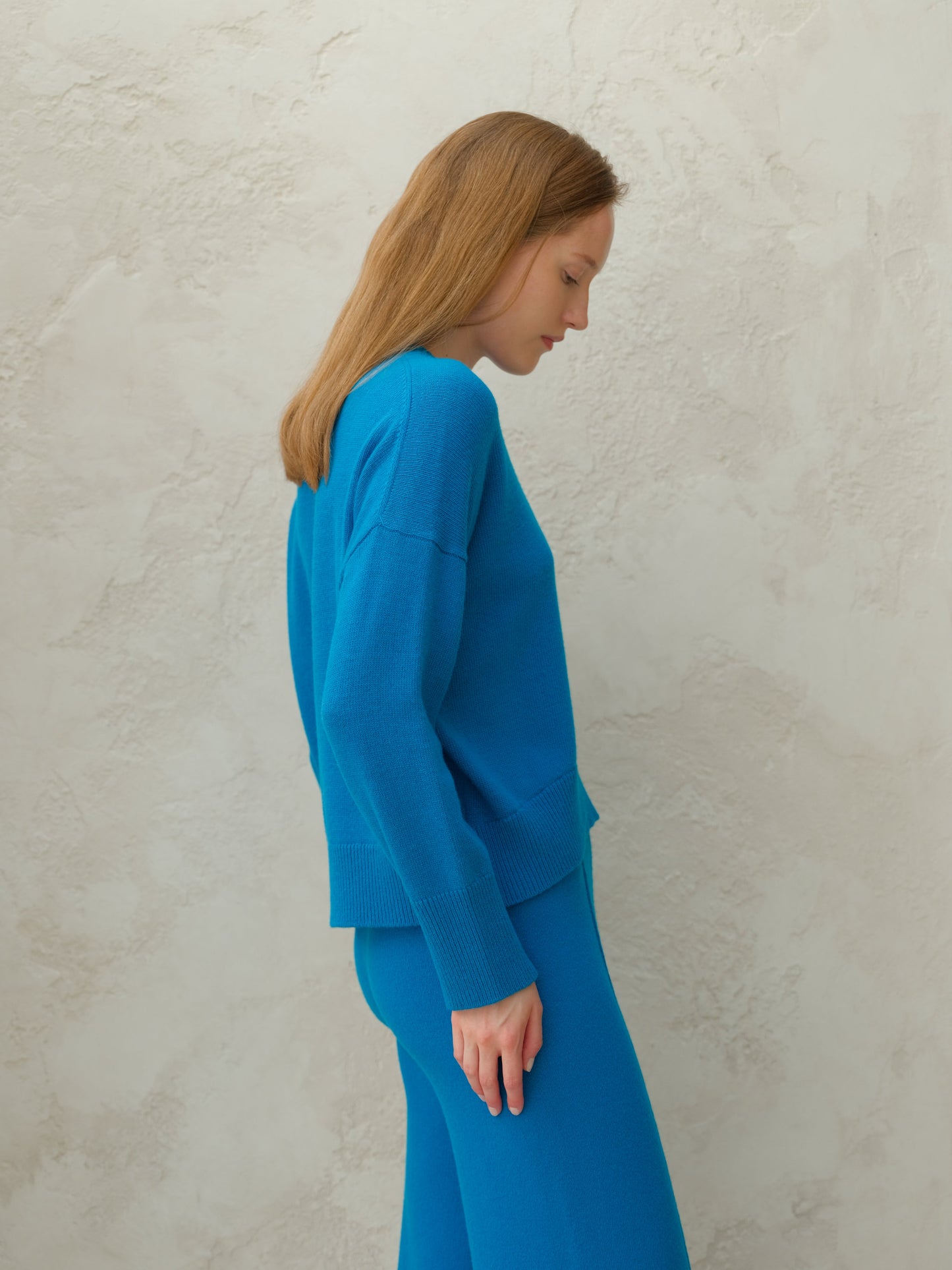 Side profile of model in blue cashmere mix crewneck sweater with matching knit pants.