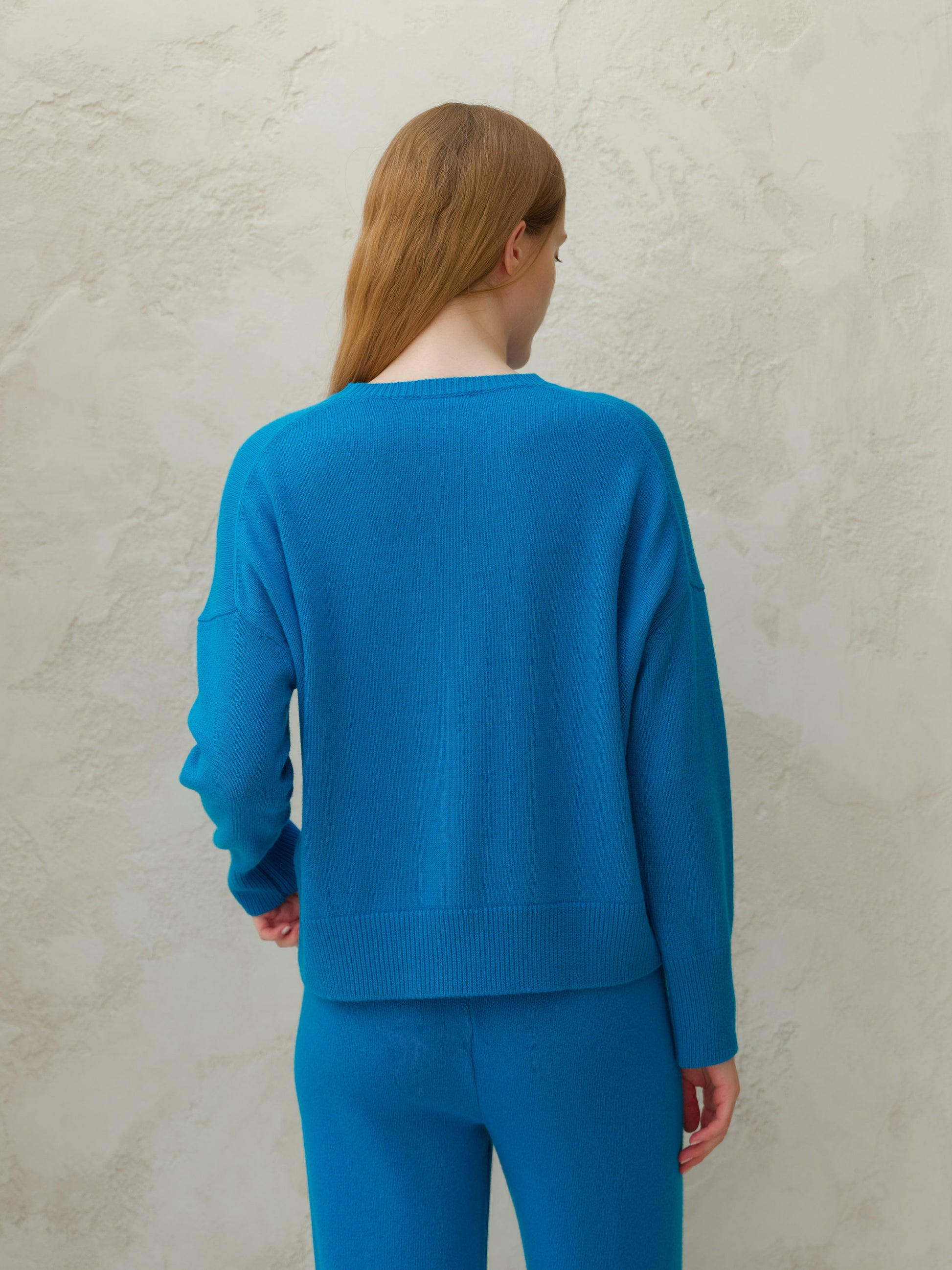 Back view of a model wearing a bright blue cashmere mix crewneck sweater with matching pants