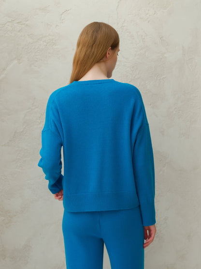 Back view of a model wearing a bright blue cashmere mix crewneck sweater with matching pants