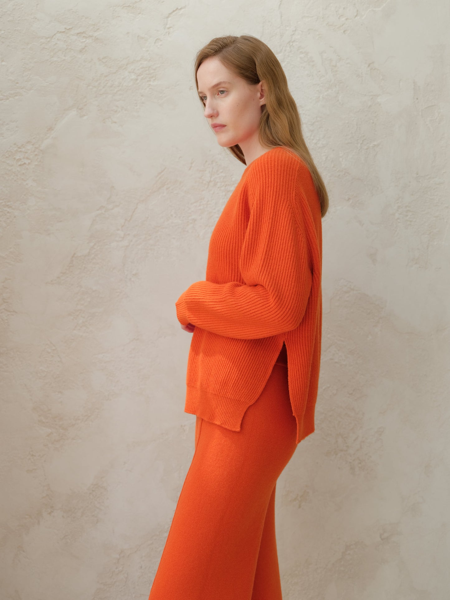 Profile view of a model in a bright orange ribbed knit sweater with matching pants.