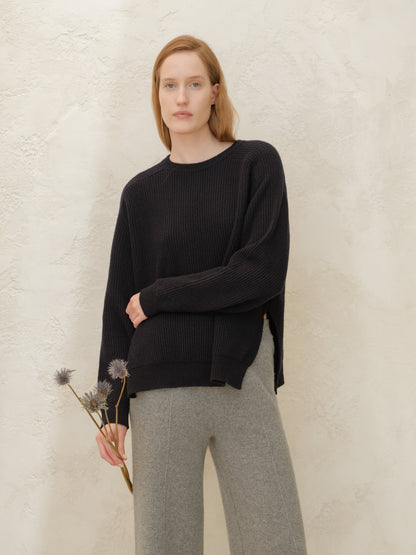Black cashmere mix crewneck ribbed sweater on a model with gray trousers in a minimalist setting