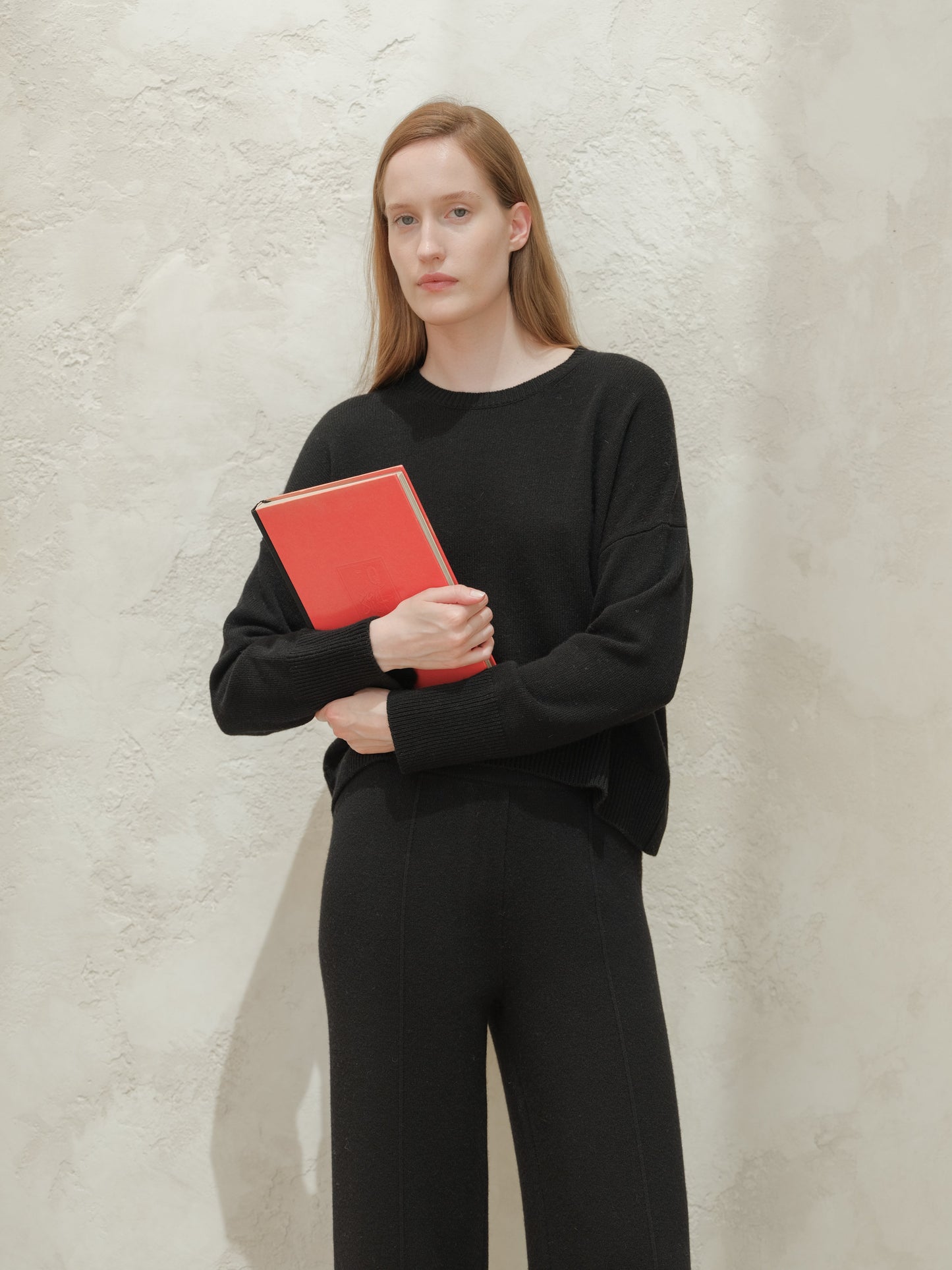 Model wearing a black cashmere mix crewneck sweater and holding a red notebook.