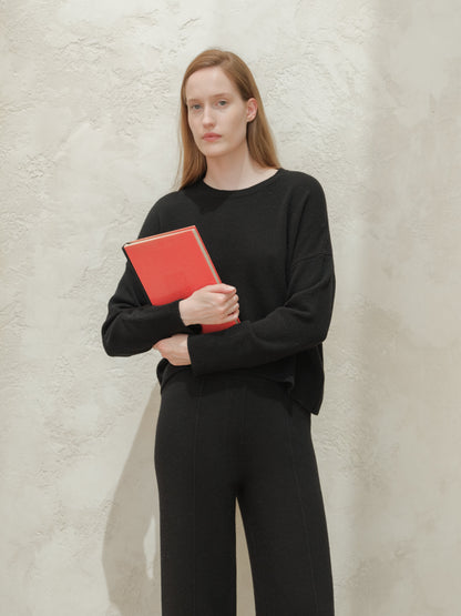 Model wearing a black cashmere mix crewneck sweater and holding a red notebook.