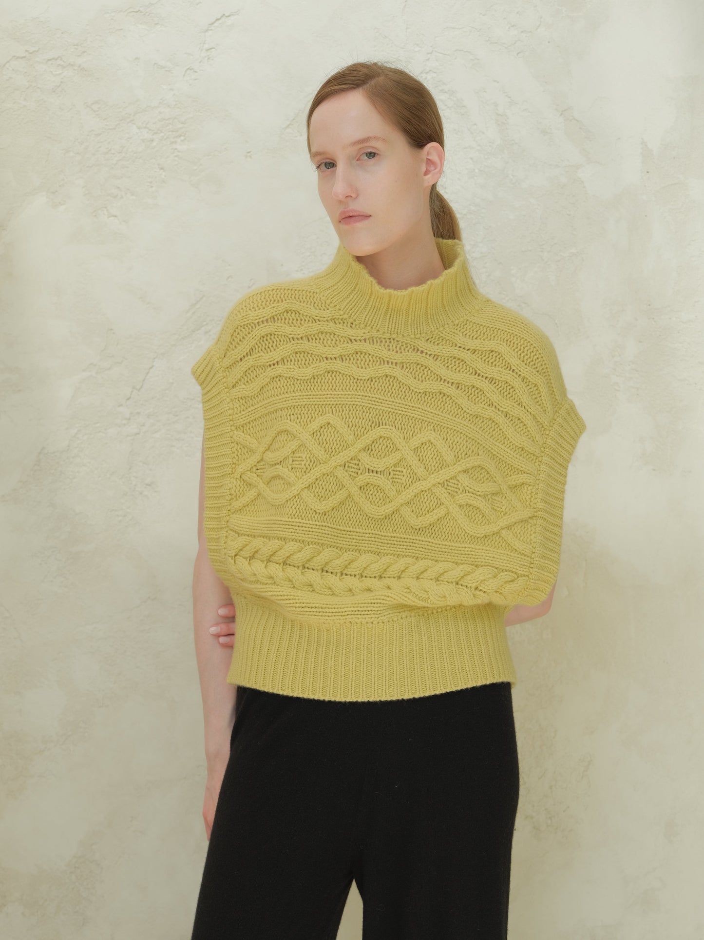 Front view of a model wearing a yellow cashmere mix maxi cable tunic with a high ribbed collar and bold cable patterns.