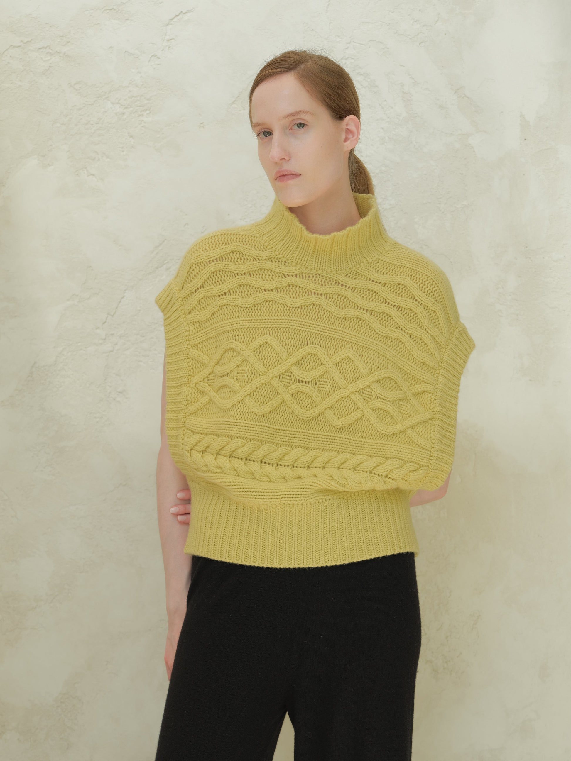 Front view of a model wearing a yellow cashmere mix maxi cable tunic with a high ribbed collar and bold cable patterns.