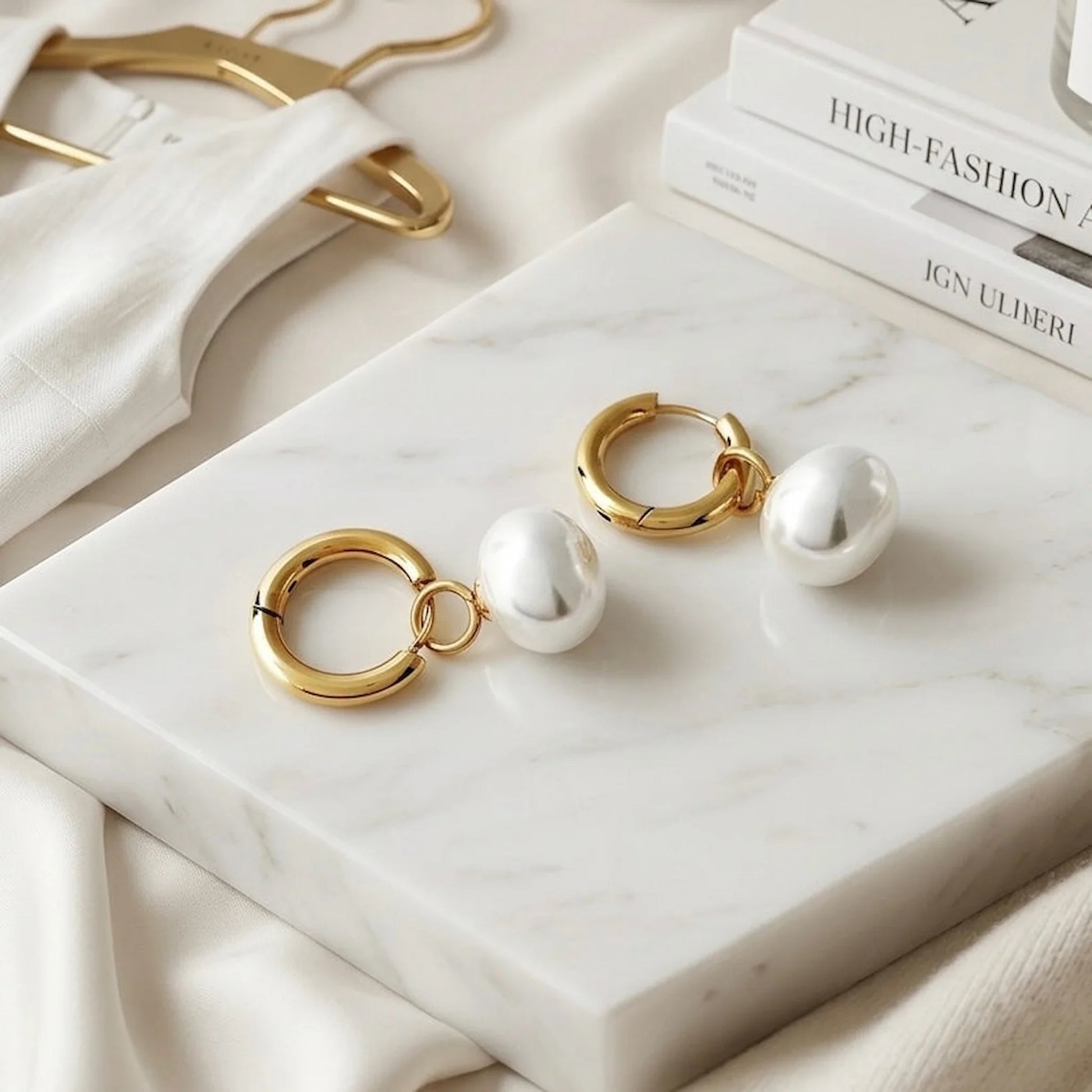 Gold and pearl earrings on a marble surface with books in the background